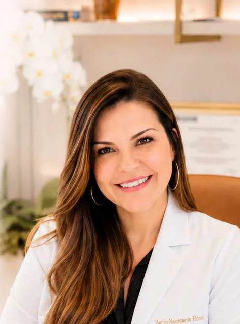 Vaniza sorrindo, de jaleco, sentada à mesa do consultório